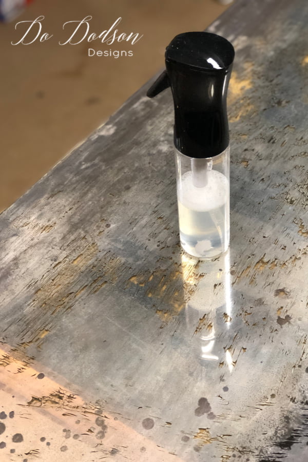 The next step in creating a DIY antique mirror is to use a solution of bleach and water 50/50 mixture in a spray bottle and lightly mist over the back of the mirror.