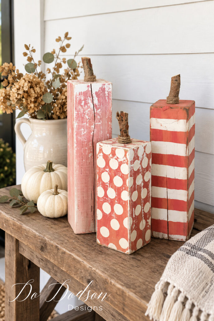 Three distressed DIY 4x4 wood pumpkins with stripes and polka dots styled on a farmhouse porch for fall.