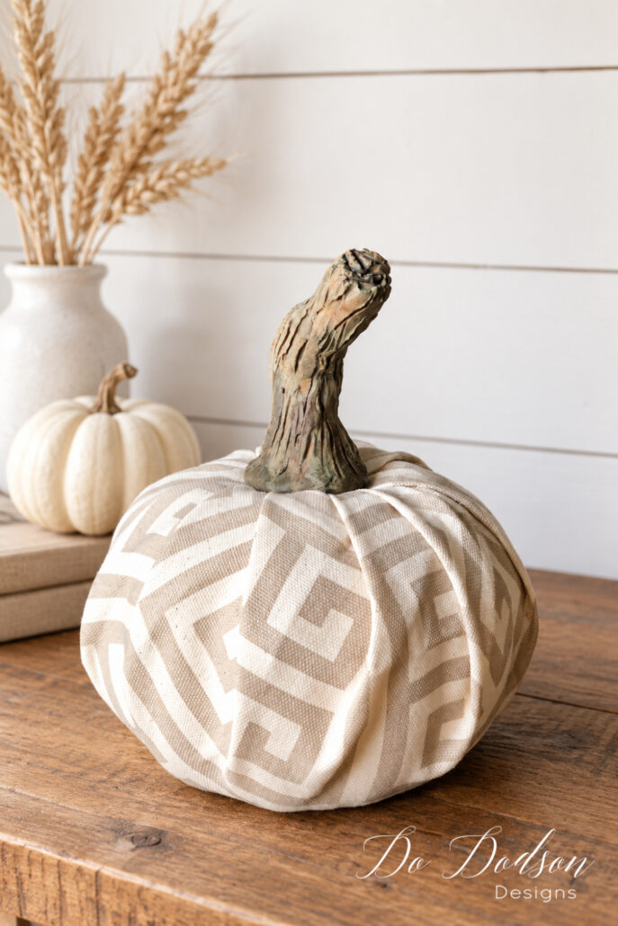 Neutral fabric pumpkin with a realistic handmade clay stem styled on a modern farmhouse table for fall
