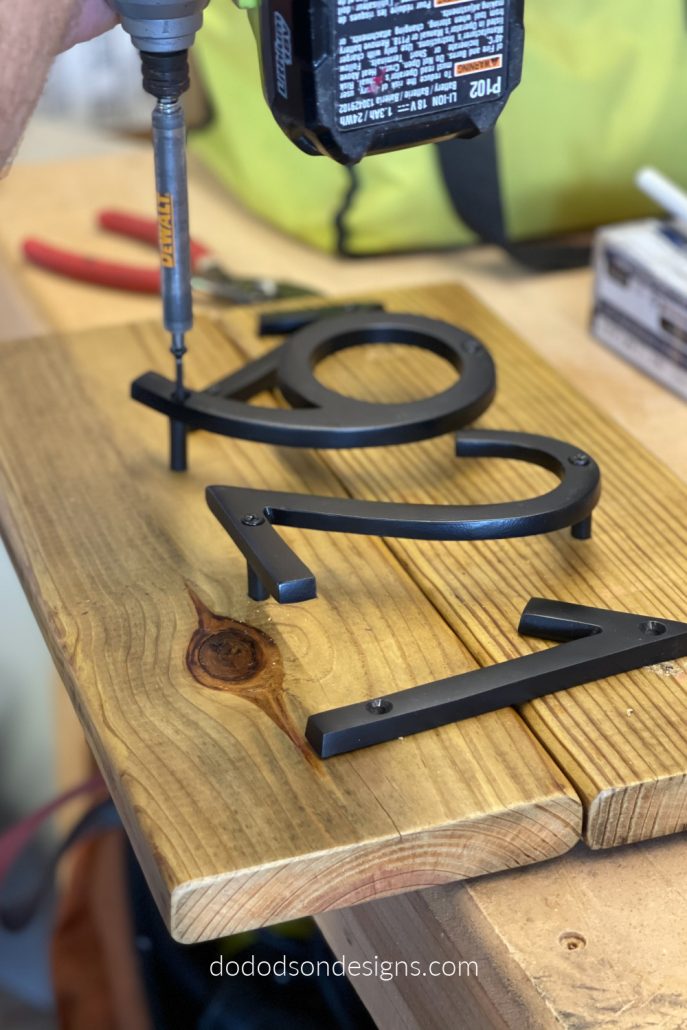 Lay the modern house numbers flat on the wood where you want them and mark the holes with a pencil first. Use a tape measure to be sure to get equal spacing. Then place the spacers under each letter and secure them with the wood screws provided. Nothing hard about that. 