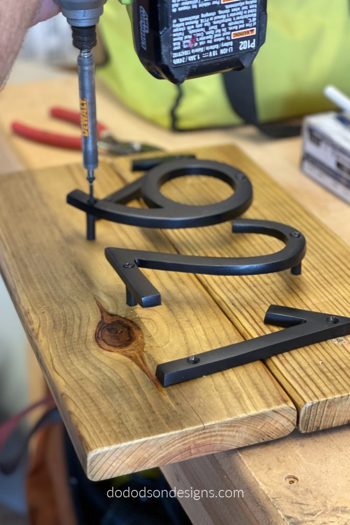 Lay the modern house numbers flat on the wood where you want them and mark the holes with a pencil first. Use a tape measure to be sure to get equal spacing. Then place the spacers under each letter and secure them with the wood screws provided. Nothing hard about that.
