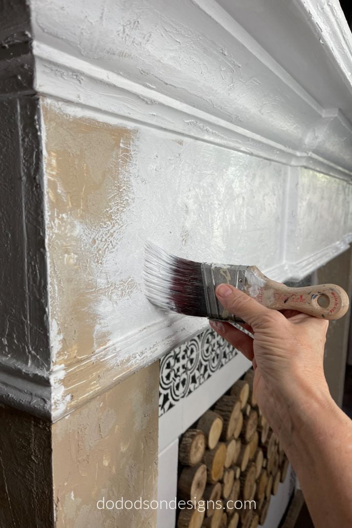 After adding the texture paint to my builder-grade fireplace mantel, I painted over the whole thing with a white chalk paint. Now, when I sand it back, I'll get a DIY chipped paint look. You got to see the finished product! It's so cool!