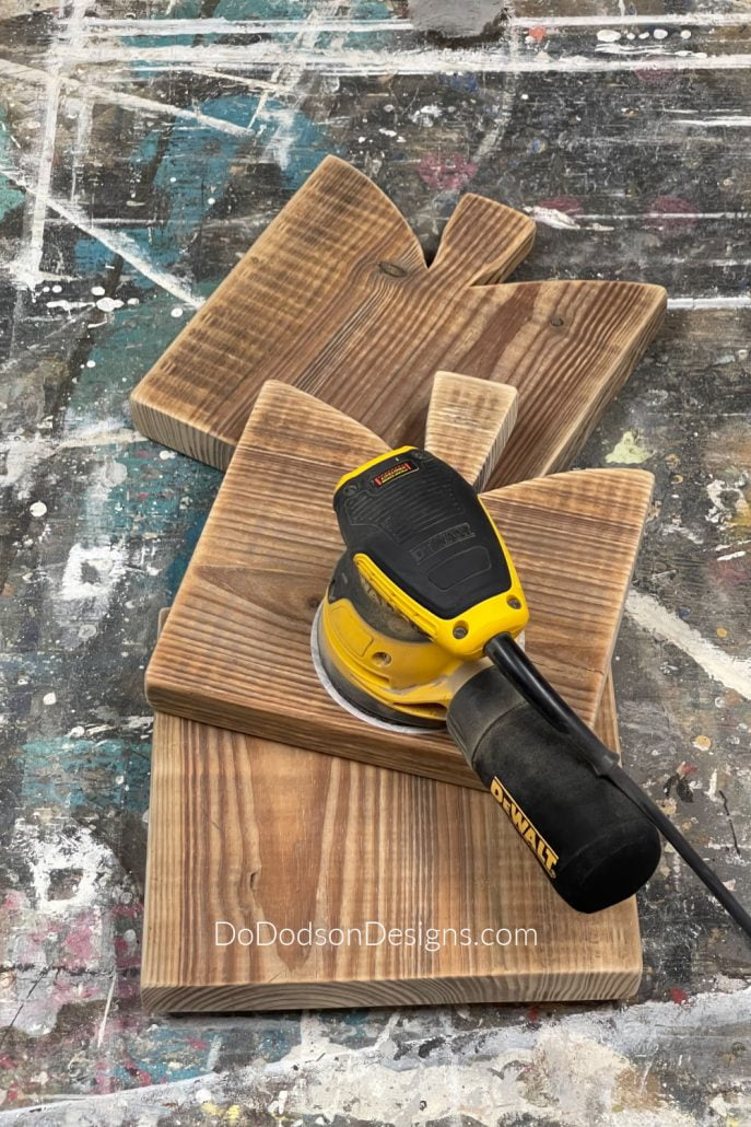 With a 220 grit sandpaper or a rotary sander, smooth the edges of the DIY table risers. If you want the edges more rounded, you can up the grit of sandpaper to 120 grit. Be sure to go back and smooth with the 220 grit after rounding. An electric sander works best for this. Learn how to DIY these amazing DIY primitive cutting boards on my blog.