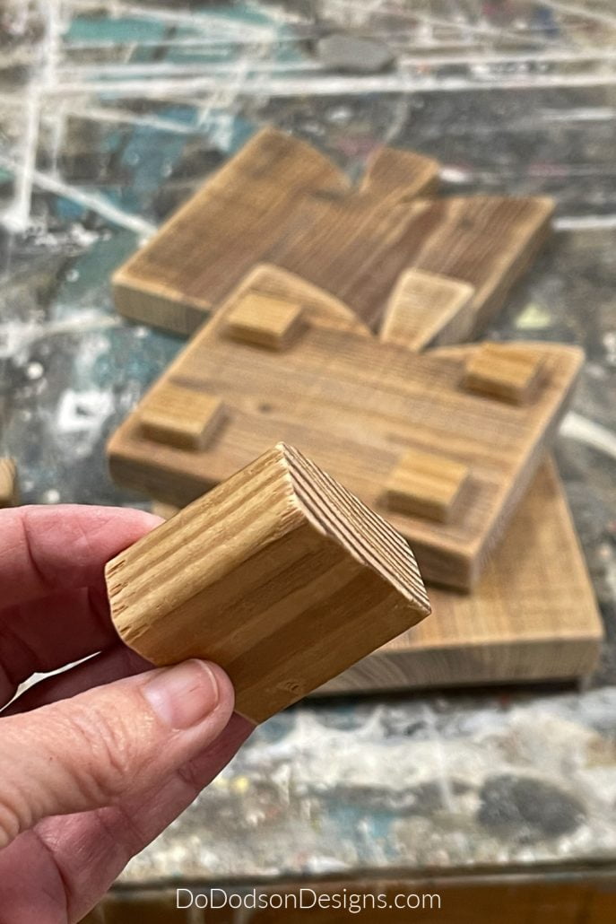 With whatever wood you have laying around, cut out 2-inch squares for the legs. Be sure to sand those like you did your table riser.