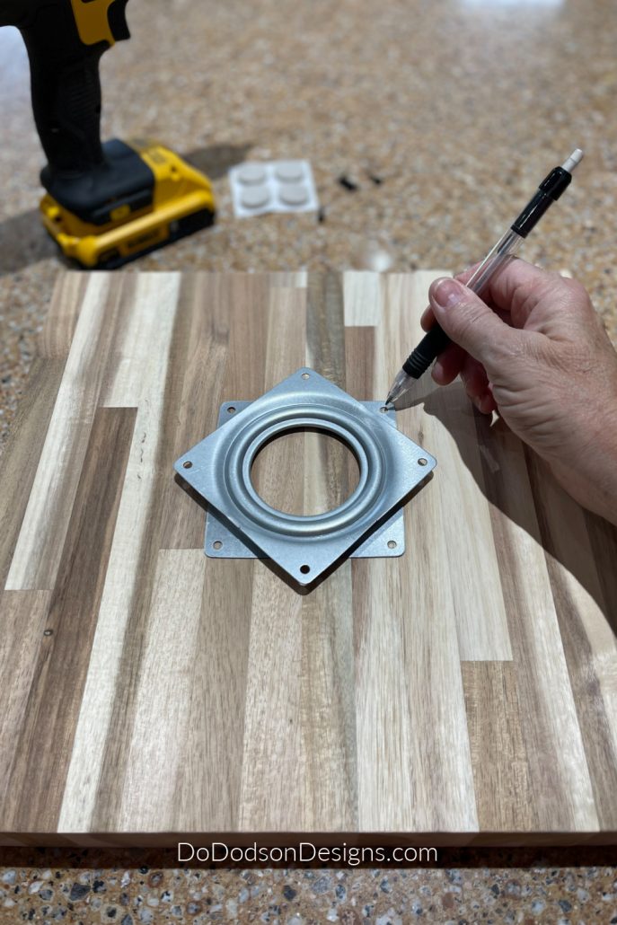 Center the lazy susan rotating turntable bearing hardware in the center of the bottom side of your board. Next, with a pencil, mark where the screws will be inserted but only on the base part of the hardware.