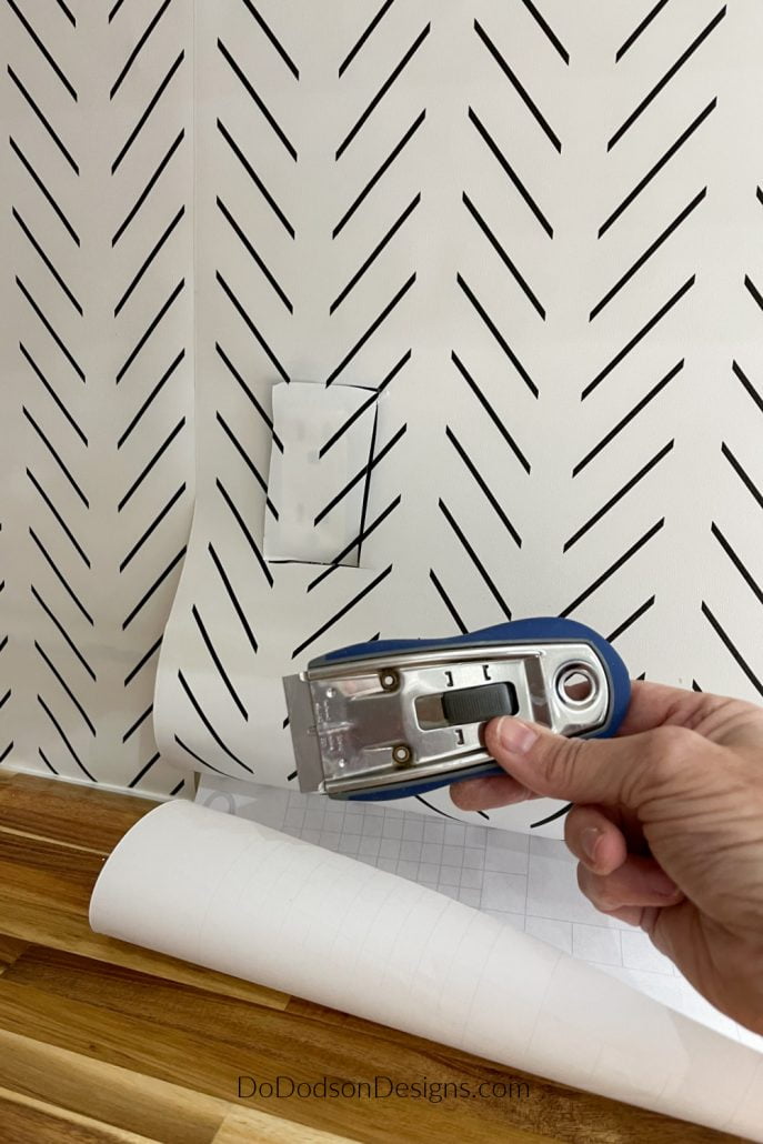Once you have the DIY peel and stick wallpaper backsplash in place, use a utility knife to carefully remove the excess at the bottom of the paper and cut around electrical outlets.