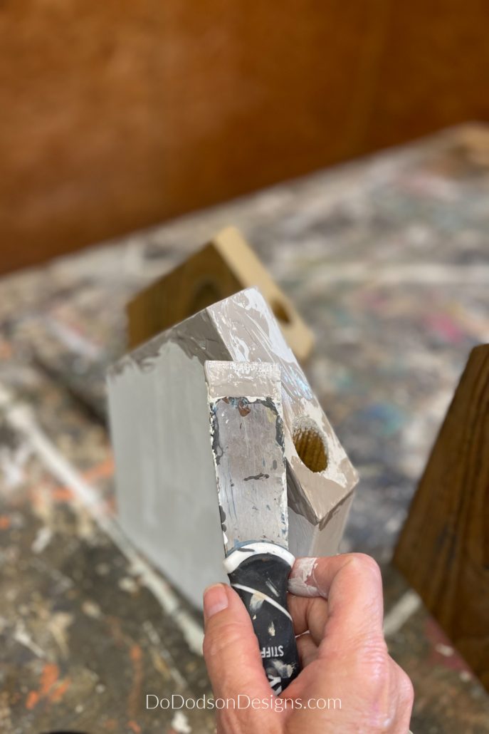 I used a paint scrapping tool to drag paint across my scrap wood block houses to create an amazing textured finish.