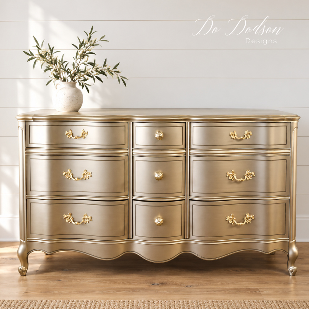French provincial dresser painted in Warm Silver metallic paint with gold hardware, styled with olive branches against a white shiplap wall.