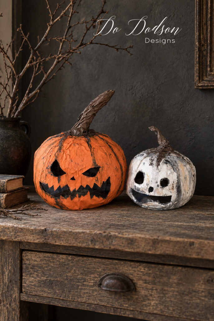 Two handmade paper mache pumpkin heads displayed on a rustic wood console as moody indoor Halloween decor.