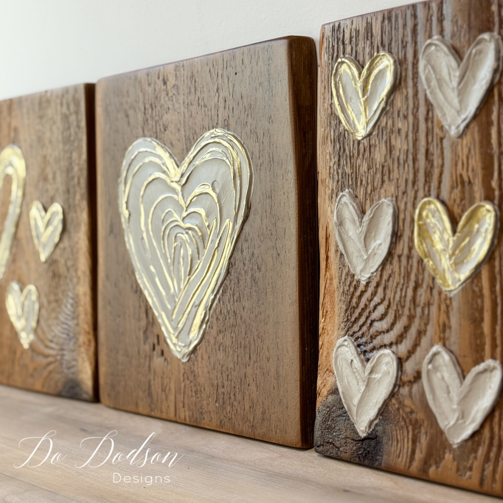 Close up of textured spackle heart art on barn wood blocks with subtle gold accents, neutral farmhouse decor.