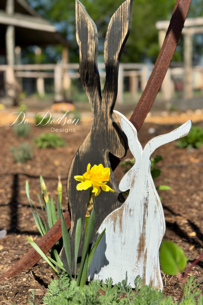 DIY wood bunny garden decor made from scrap wood displayed in a flower bed with a yellow bloom, adding rustic farmhouse charm to outdoor spring landscaping.