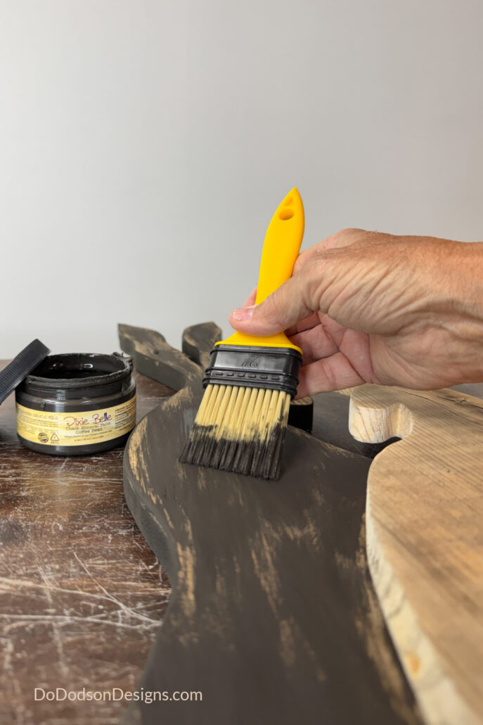 Applying dark brown chalk paint to a DIY wood Easter bunny cutout made from scrap wood using a paintbrush, showing rustic farmhouse finish technique.