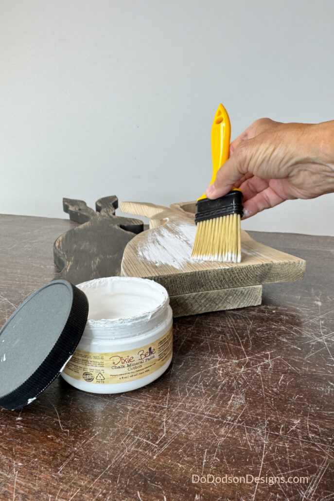 Applying white chalk paint to a DIY wood Easter bunny made from scrap wood, creating a rustic farmhouse finish with a paintbrush.