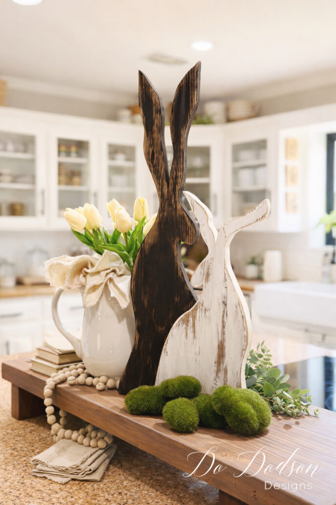 Finished DIY wood Easter bunnies styled on a farmhouse kitchen island with tulips, moss balls, and neutral decor for spring decorating inspiration.