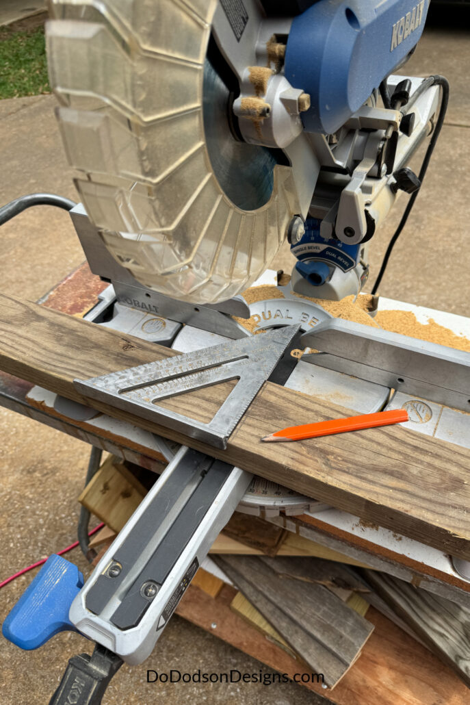 Cutting a 2x4 board on a miter saw using a speed square and pencil for accurate measurements during a wood bench build.
