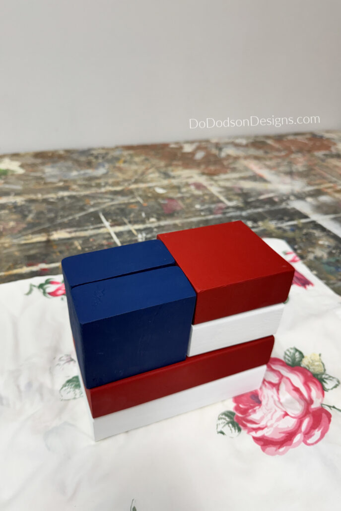 Handmade patriotic DIY wood block crafts painted red, white, and blue and arranged to resemble an American flag using scrap 2x4 wood pieces for farmhouse-style 4th of July decor.