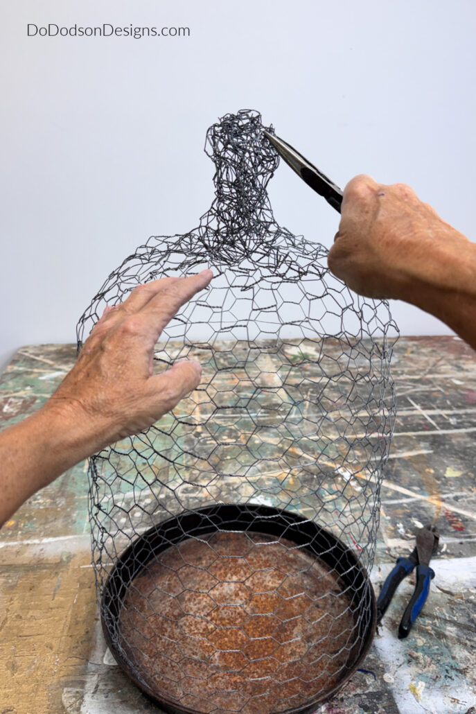 DIY chicken wire cloche as needle-nose pliers tighten and shape the twisted wire knob at the top. This final step completes the handmade garden cloche DIY project, creating a rustic chicken wire cage that protects plants while adding charming farmhouse style to the garden or home décor.