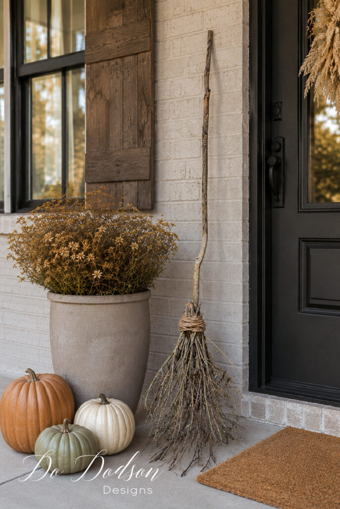 DIY witch&rsquo;s broom made from branches and jute rope styled with pumpkins and rustic fall decor on a front porch.