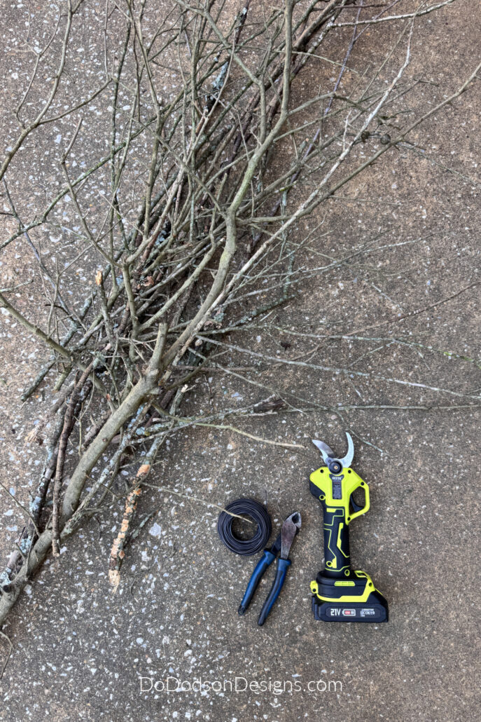 Branches, pruning shears, wire, and wire cutters gathered to make a rustic DIY witch&rsquo;s broom for Halloween decor.
