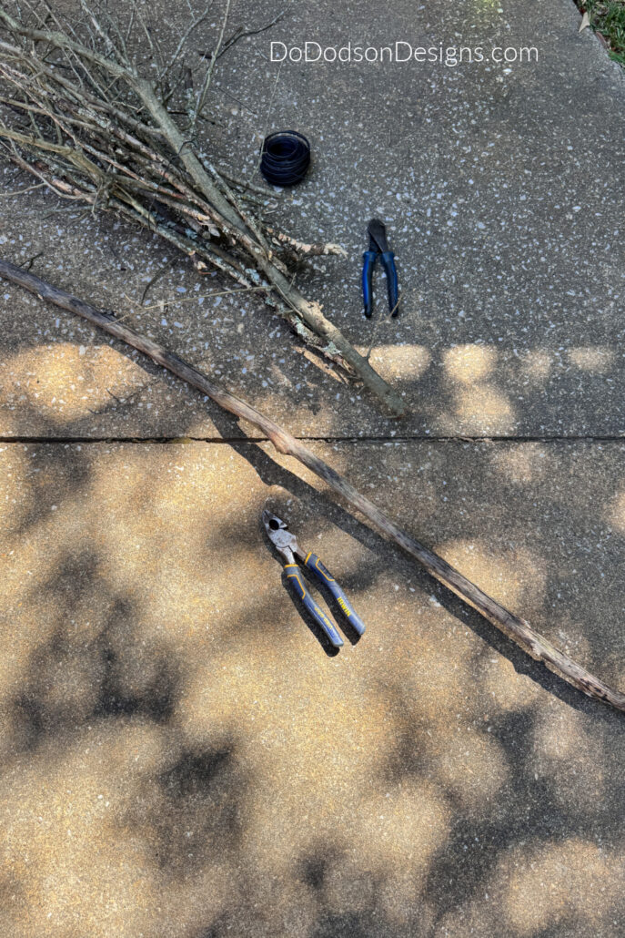 Long natural branch selected for the broomstick handle beside bundled twigs, wire, and cutters for a DIY witch&rsquo;s broom.