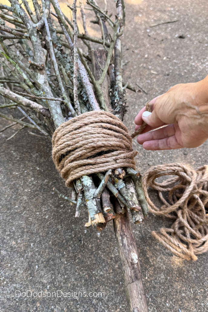Wrapping jute rope around bundled branches and a natural wood handle to finish a rustic DIY witch&rsquo;s broom.