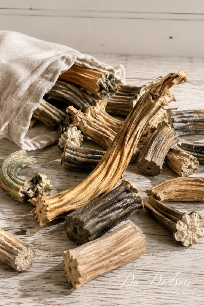 Dried real pumpkin stems spilling from a natural linen bag across a weathered farmhouse table.
