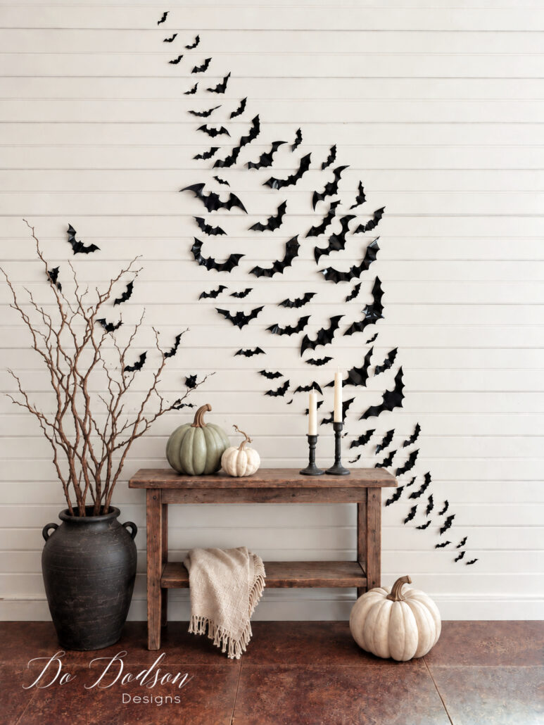Sweeping Halloween bat wall above a rustic wood console styled with black candlesticks, neutral pumpkins, and bare branches.