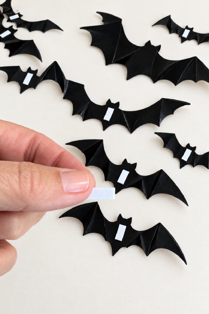 Adding double-sided adhesive strips to the backs of 3D PVC bats for a Halloween bat wall.