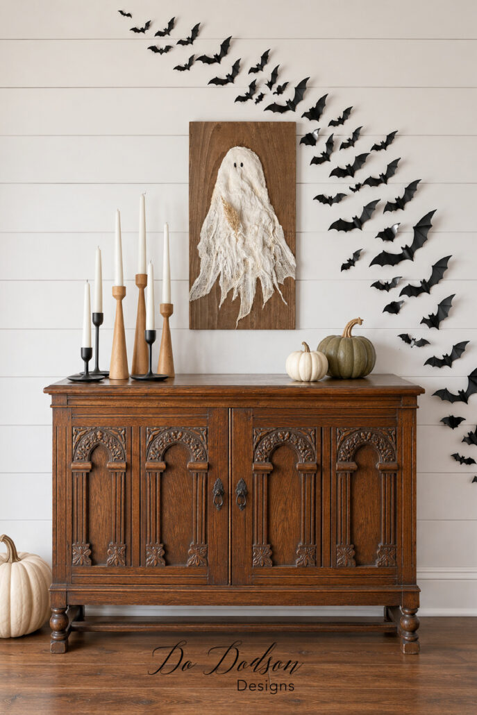Full Halloween bat wall displayed above an antique carved cabinet with ghost artwork and neutral pumpkins.