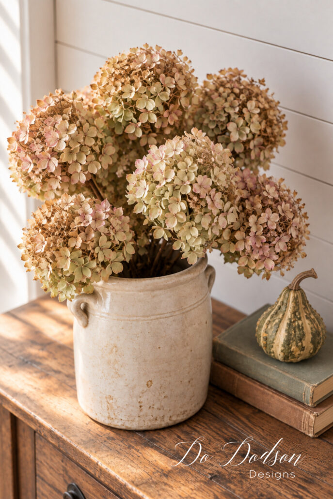 Dried blush and green hydrangeas arranged in a vintage crock with a natural fall gourd