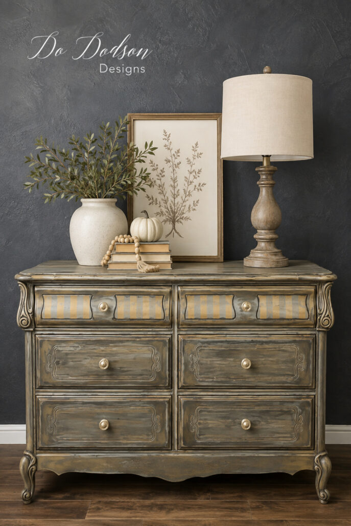 French Provincial dresser makeover with a layered distressed paint finish, striped drawer details, and brass hardware styled against a dark farmhouse wall.