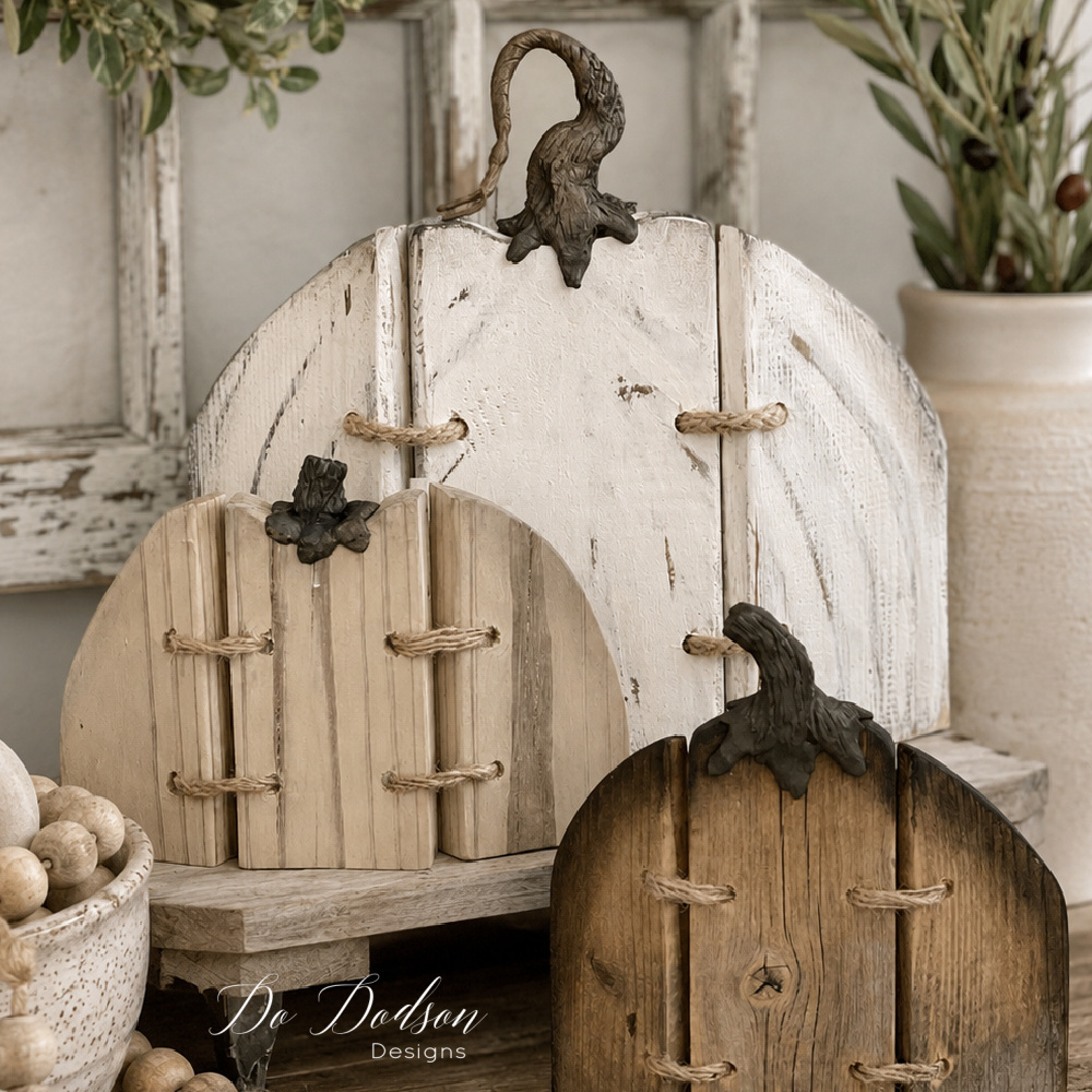 Three rustic wood pumpkins in white, beige, and brown, joined with twine and topped with curved stems, arranged in a neutral fall display.