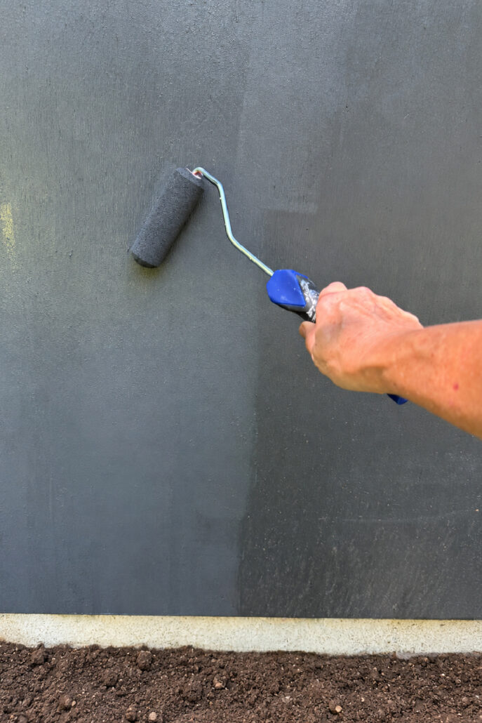 Hand applying Sherwin-Williams Iron Ore exterior paint to a farmhouse shed with a small roller.