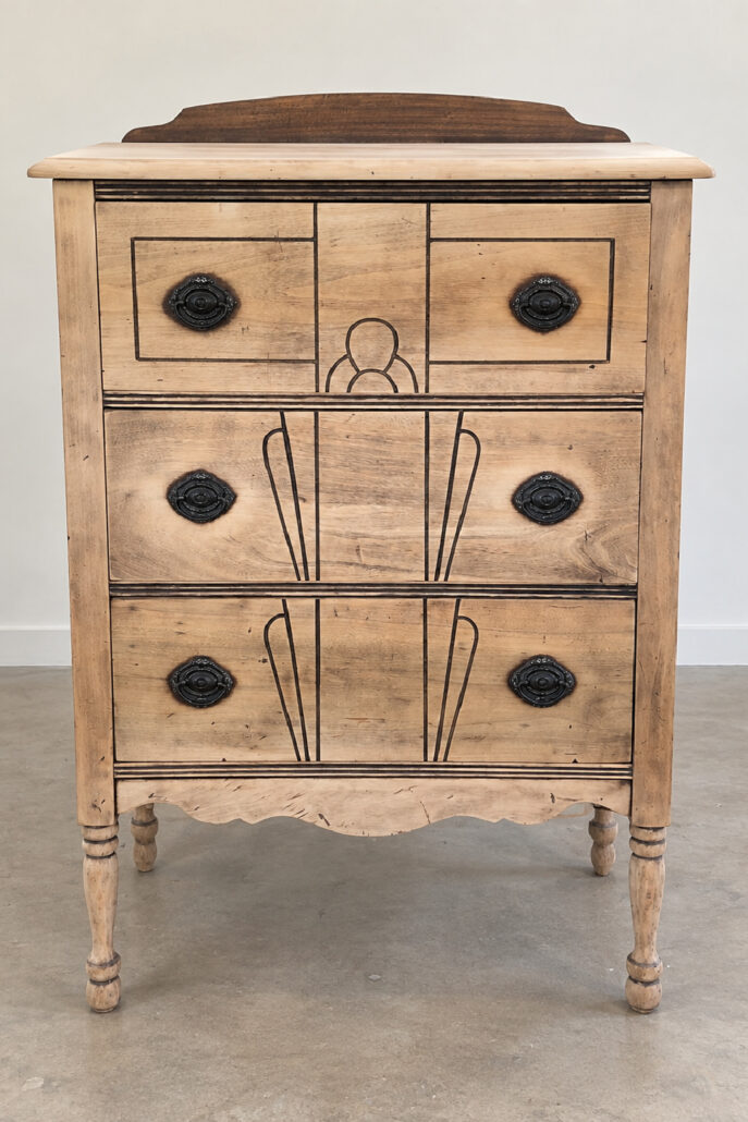 Thrifted wood chest after cleaning and sanding, with bare wood, dark decorative details, and original drawer hardware ready for refinishing.