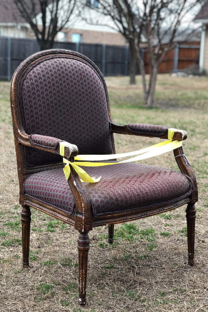Vintage French armchair with worn upholstery and yellow caution tape before its thrift store furniture makeover.