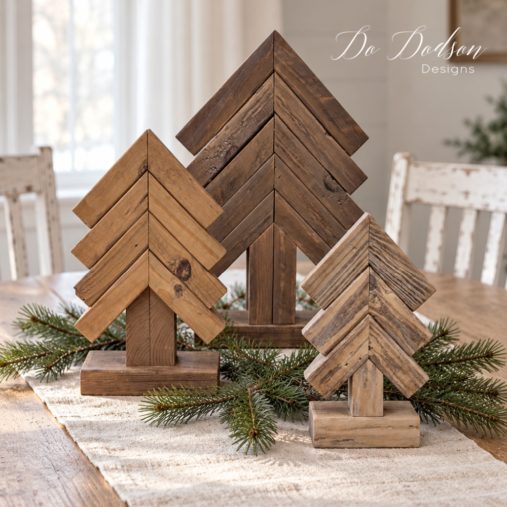 Three 2x4 scrap wood Christmas trees in contrasting colorwash finishes arranged with pine branches on an ivory runner as a dining table centerpiece.