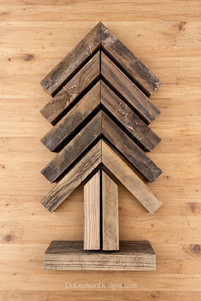 Angled 2x4 pieces arranged into a Christmas tree shape with a wood trunk and base before assembly.