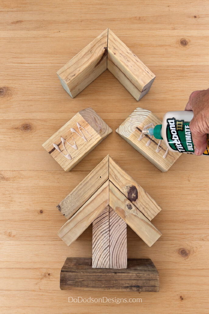 Applying wood glue to cut 2x4 pieces for a scrap wood Christmas tree.